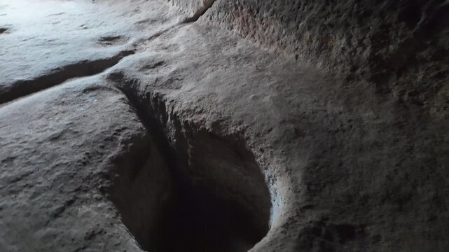 The slow movement of the camera shows an ancient mortar and pestle embedded in the stone floor of the cave, showing details of a primitive tool for grinding Vardzia grains, seeds or minerals