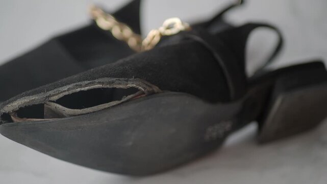Close up motion of a broken black suede shoe with a gold chain accessory revealing its damaged sole and interior parts