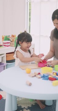 Asian mother and daughter playing kitchen pretend game, cutting toy vegetables on a wooden board.