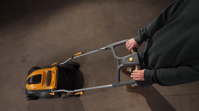 High angle view person holding the handle of an electric lawn mower, preparing for or performing yard work and garden maintenance