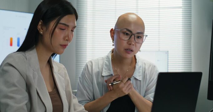 Two coworkers collaborate over a computer and paperwork to brainstorm marketing ideas and scope a new startup project.