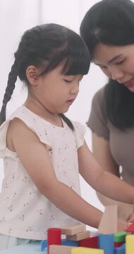Asian little girl playing with educational wooden toys at table with her mother.