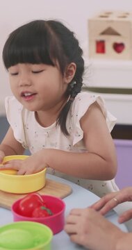 Asian mother and little daughter sorting plastic toy food into colorful bowls.