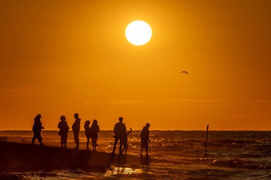 Saint-Aubin-Sur-Mer, France - 07 27 2026: View people on the jetty, the beach, the sea and the sun at golden hour
