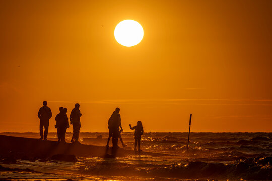 Saint-Aubin-Sur-Mer, France - 07 27 2026: View people on the jetty, the beach, the sea and the sun at golden hour