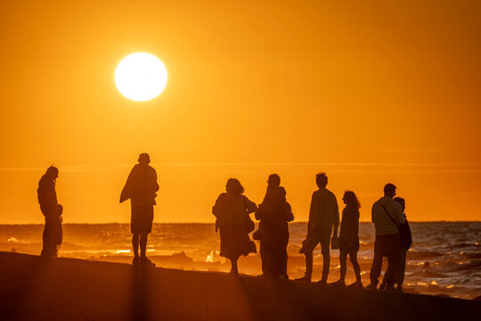Saint-Aubin-Sur-Mer, France - 07 27 2026: View people on the jetty, the beach, the sea and the sun at golden hour