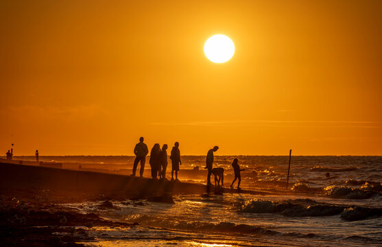 Saint-Aubin-Sur-Mer, France - 07 27 2026: View people on the jetty, the beach, the sea and the sun at golden hour
