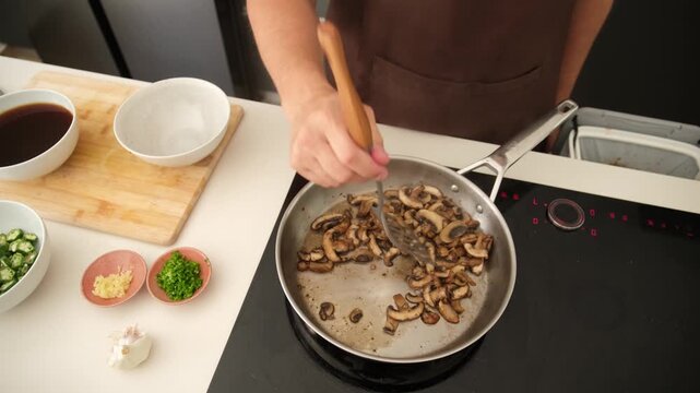 Professional cook frying shiitake mushrooms on an induction stove in a modern kitchen