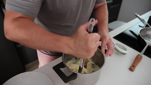 Close up of male hands making mashed potatoes with a masher in a modern kitchen