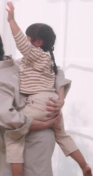 Happy Asian mother giving piggyback ride to her daughter in living room.