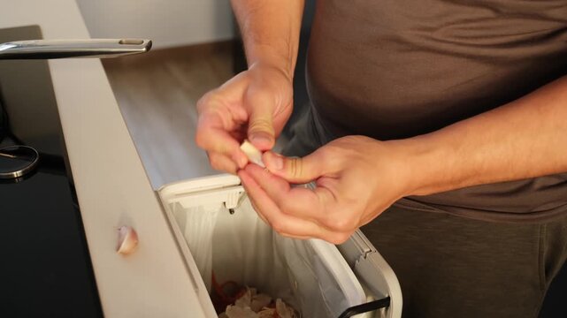 Male hands peeling fresh garlic and throwing the skin into a built in countertop compost bin