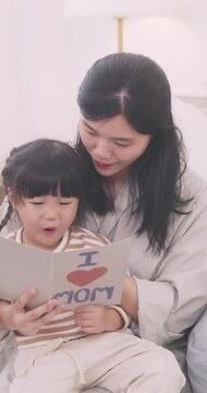 Asian little girl reading Mother's Day greeting card with her mother at home.