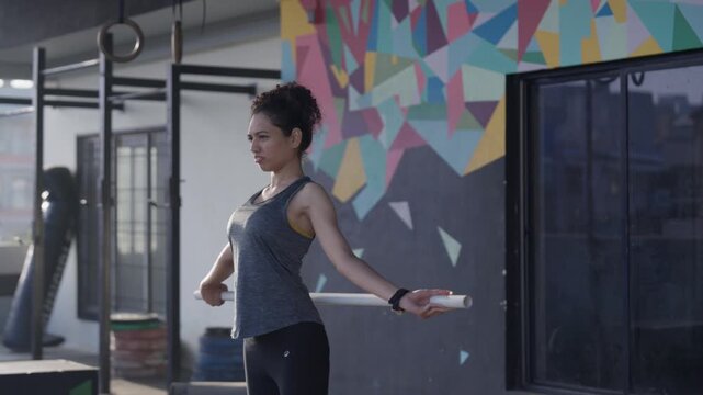 South Asian female athlete performs PVC shoulder pass throughs with a dowel rod during shoulder mobility training in a modern indoor gym. Collection: WORKOUTSERIES2026.