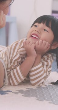 Close up of cute Asian little girl lying on mat smiling and talking to mother.