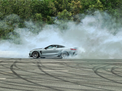 Sports car drifting and burning rubber on an asphalt track creating thick smoke for a high performance automotive concept