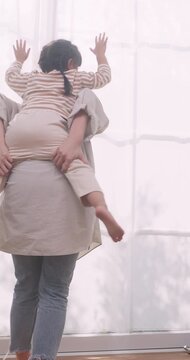 Happy Asian mother giving piggyback ride to her daughter in living room.