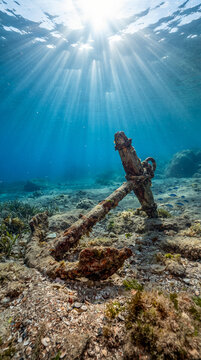 Antigua ancla oxidada sobre el fondo marino iluminada por rayos de sol que atraviesan el agua cristalina. Escena submarina tropical de gran realismo y serenidad.