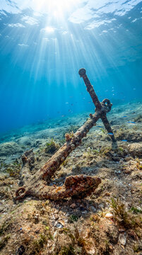 Antigua ancla oxidada sobre el fondo marino iluminada por rayos de sol que atraviesan el agua cristalina. Escena submarina tropical de gran realismo y serenidad.