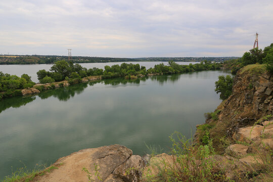 Serene lake with rocky shores and lush green trees under a cloudy sky