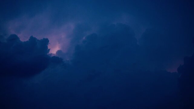 Ominous dark blue storm clouds gathering in the night sky, illuminated from within by continuous flashes of purple and white lightning during a dramatic and intense electrical weather event