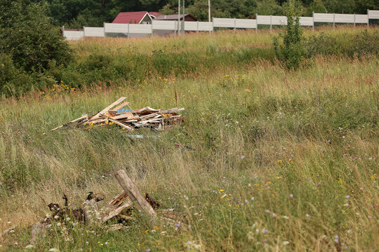  Illegal garbage dump of old furniture on a green hill near a dirt road, with new residential buildings in the background. Concept of environment pollution, illegal waste dumping and social issues now
