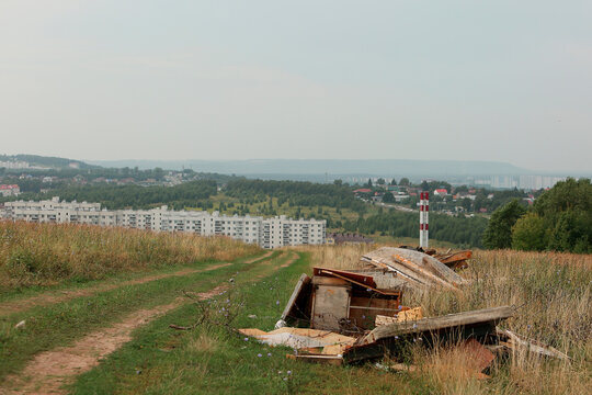  Illegal garbage dump of old furniture on a green hill near a dirt road, with new residential buildings in the background. Concept of environment pollution, illegal waste dumping and social issues now