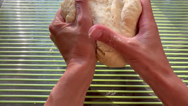 Close-up of hands kneading raw dough on a green striped baking mat in bright sunlight