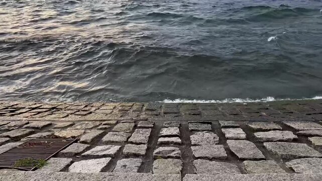 Stone embankment with waves washing onto a lakeside shoreline at sunset. Waterfront landscape and natural water movement express concepts of travel, tranquillity, and coastal resilience.
