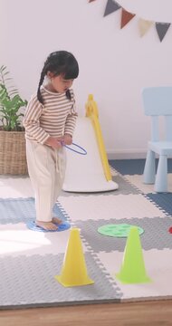 Happy Asian mother and little girl playing ring toss game together on the floor at home.