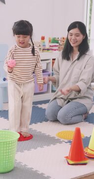 Asian mother and little girl playing sensory stepping mat game tossing balls in basket at home.