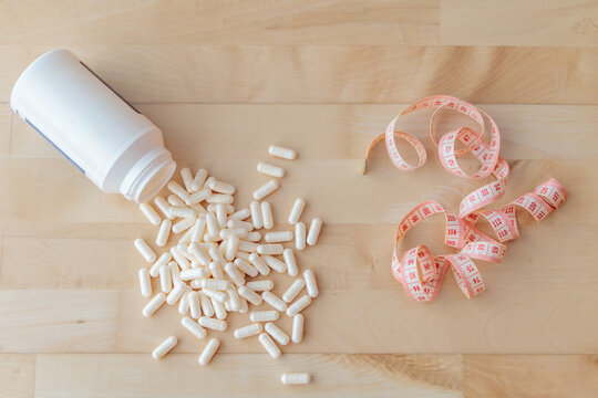White Dietary Supplement Capsules with Measuring Tape on Wooden Background, Weight Loss and Fitness Concept
