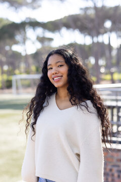Female child standing on grassy sports field wearing cream sweater near soccer goal and bleachers