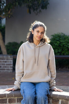 African American youth female sitting on brick ledge in courtyard, looking at camera wearing hoodie