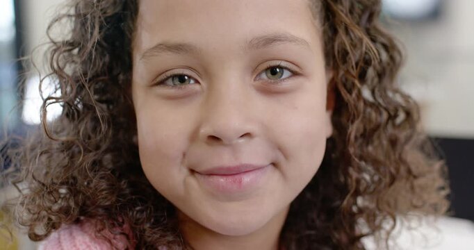 African American girl child smiling and blinking while facing camera at home in pink sweater