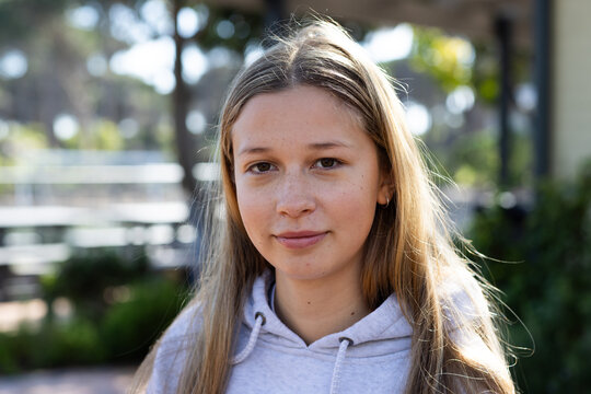 Teenage female facing camera, wearing gray hoodie with drawstrings and hoop earring in courtyard