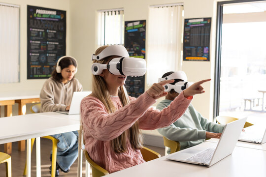 African American teens using white VR headsets, center female reaching pointing in classroom