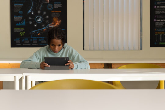 African male youth studying at white table in classroom using tablet in folio, wearing mint sweater