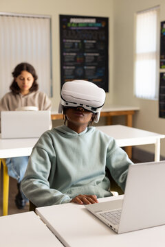 African American students in classroom in hoodies, front using VR headset, laptop, back holding cup