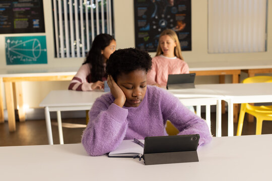 Diverse teenage female students studying in classroom with lavender sweater student using tablet