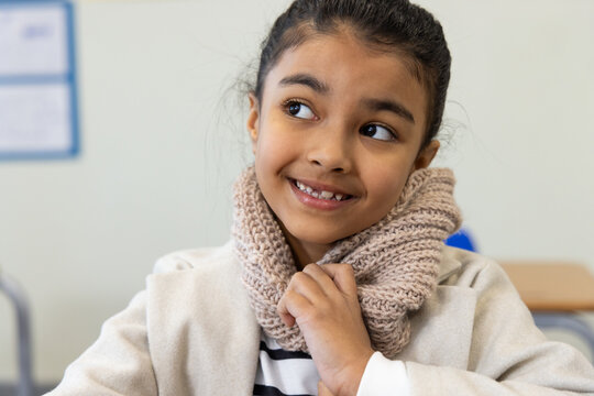 African American teenage female student sitting at school desk wearing beige knitted scarf and coat