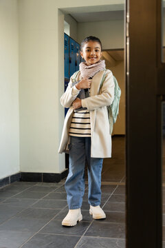African American schoolgirl standing in corridor holding mint-green backpack, blue lockers behind