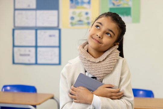 African American youth female student standing, holding tablet in coat and scarf in classroom