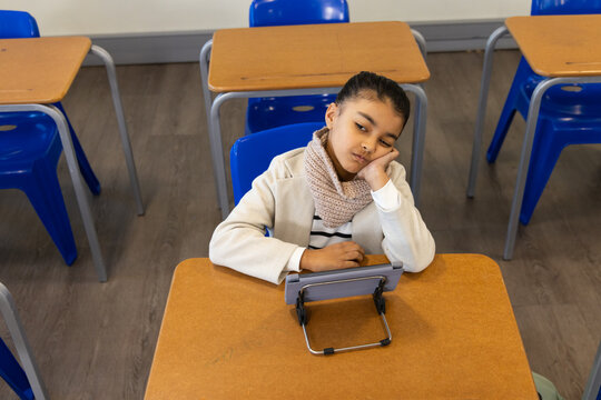 African American female child sitting at wood desk in class wearing coat, scarf, tablet on stand