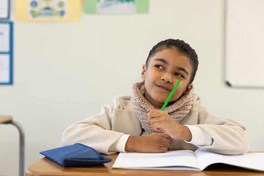 African American child sitting in classroom wearing coat scarf holding green pencil with notebook