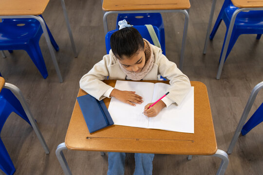 African American youth writing in notebook at desk in classroom with pink pencil and pencil case