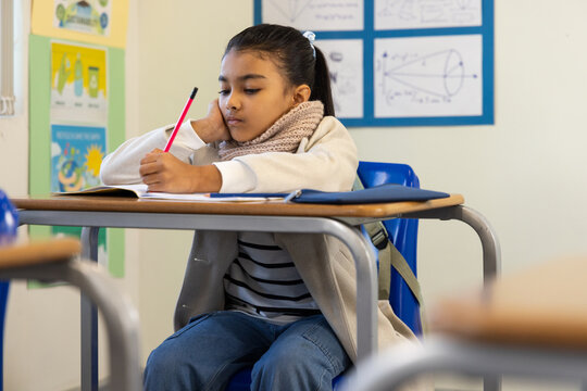 African American school child writing in notebook at classroom desk with blue folder and red pencil