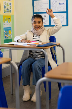 African teenage student sitting in classroom at desk in blue chair writing in open notebook