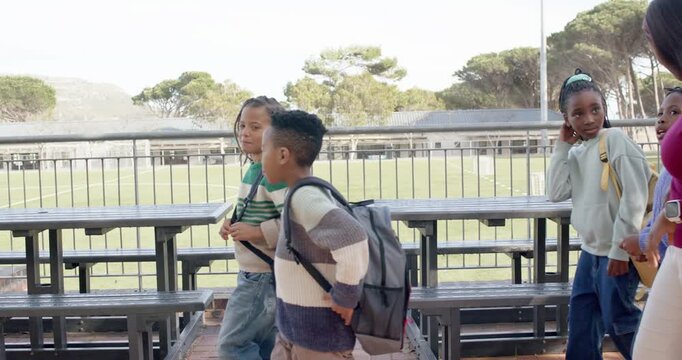 African American school group walking brick path past benches, following teacher gesturing, guiding
