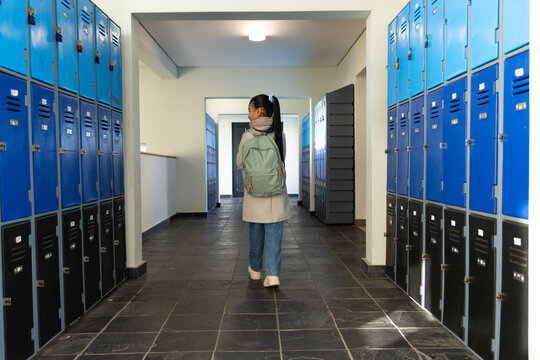Youth African American female student walking down school blue locker hall carrying green backpack