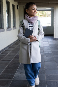 African American girl child standing in school corridor holding dark tablet wearing mint backpack